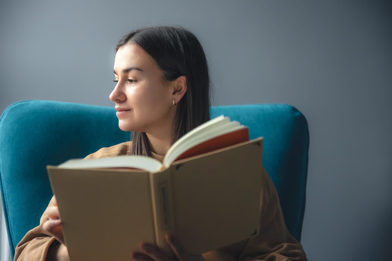 Leitora em uma poltrona, absorta na leitura de um livro de capa dura