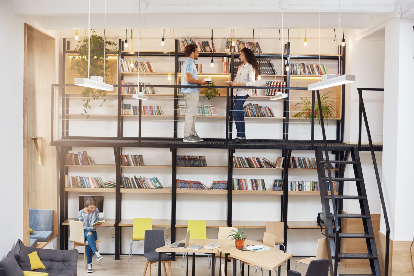 Loja com dois andares de estantes cheias de livros, onde clientes conversam e uma leitora estuda em uma mesa